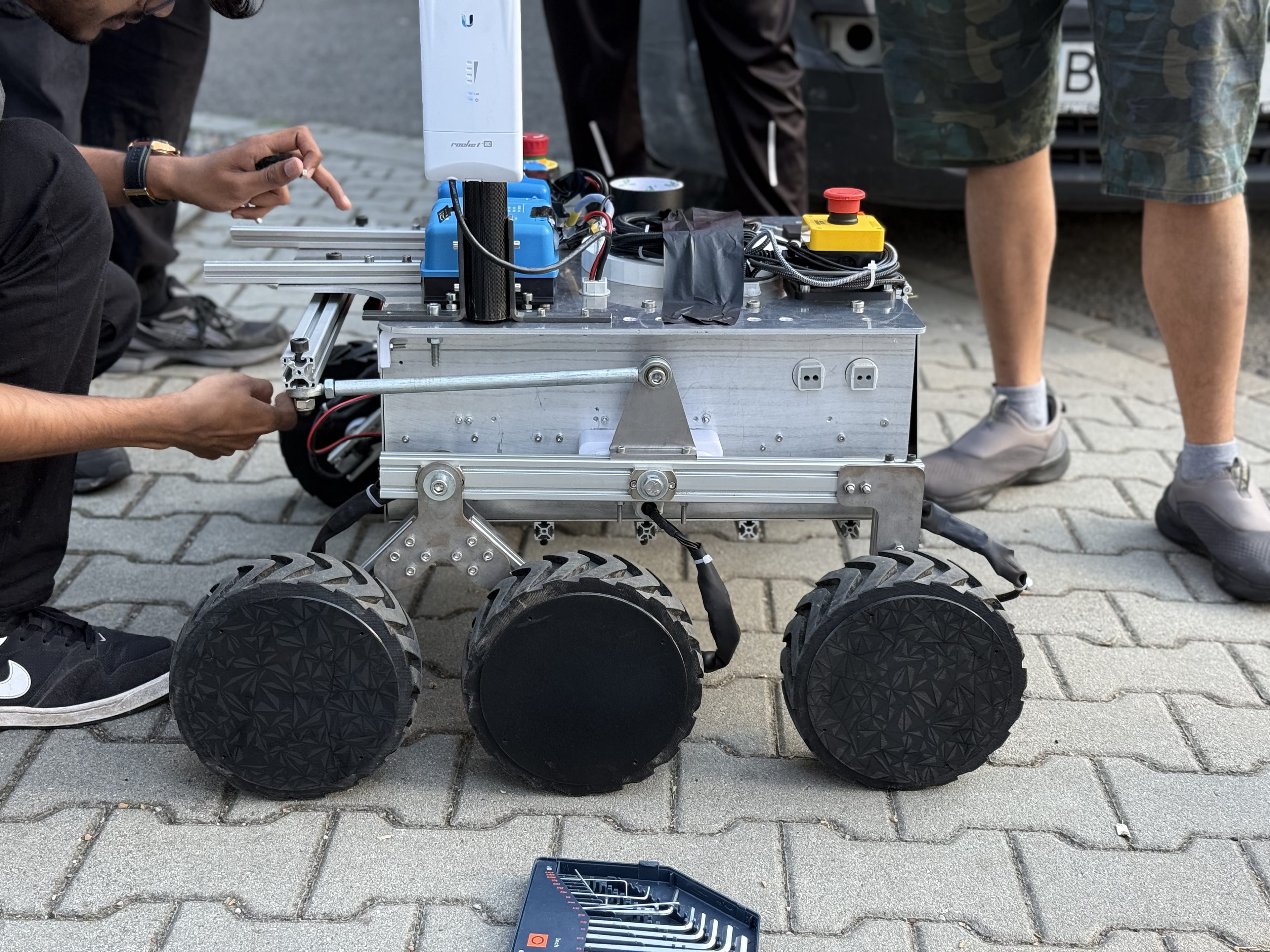 A team member fastens the suspension of the bare LEAP-One chassis on the pavement with a hex key set beside it.