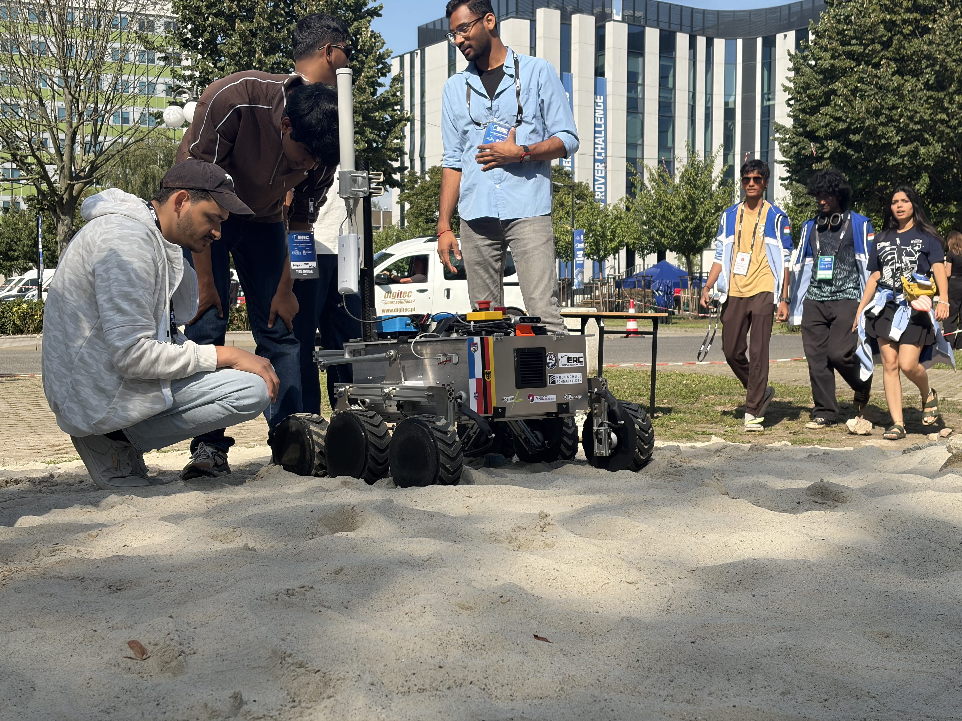 Team members crouch beside LEAP-One as it drives onto the sand of the Mars yard for a test run.