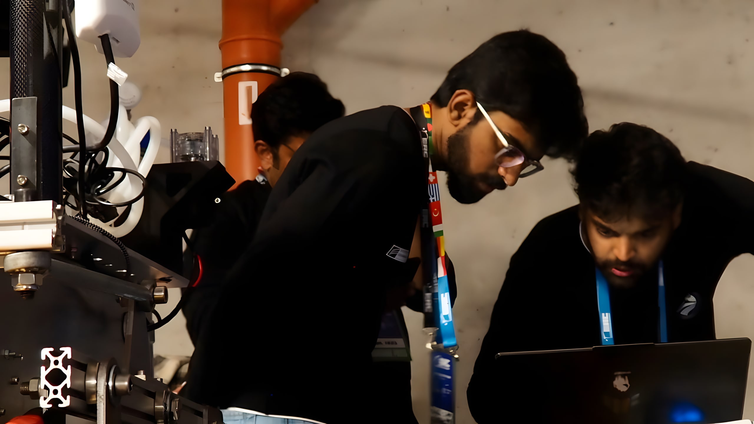 Two team members lean over a laptop beside LEAP-One's mast in the indoor hall.