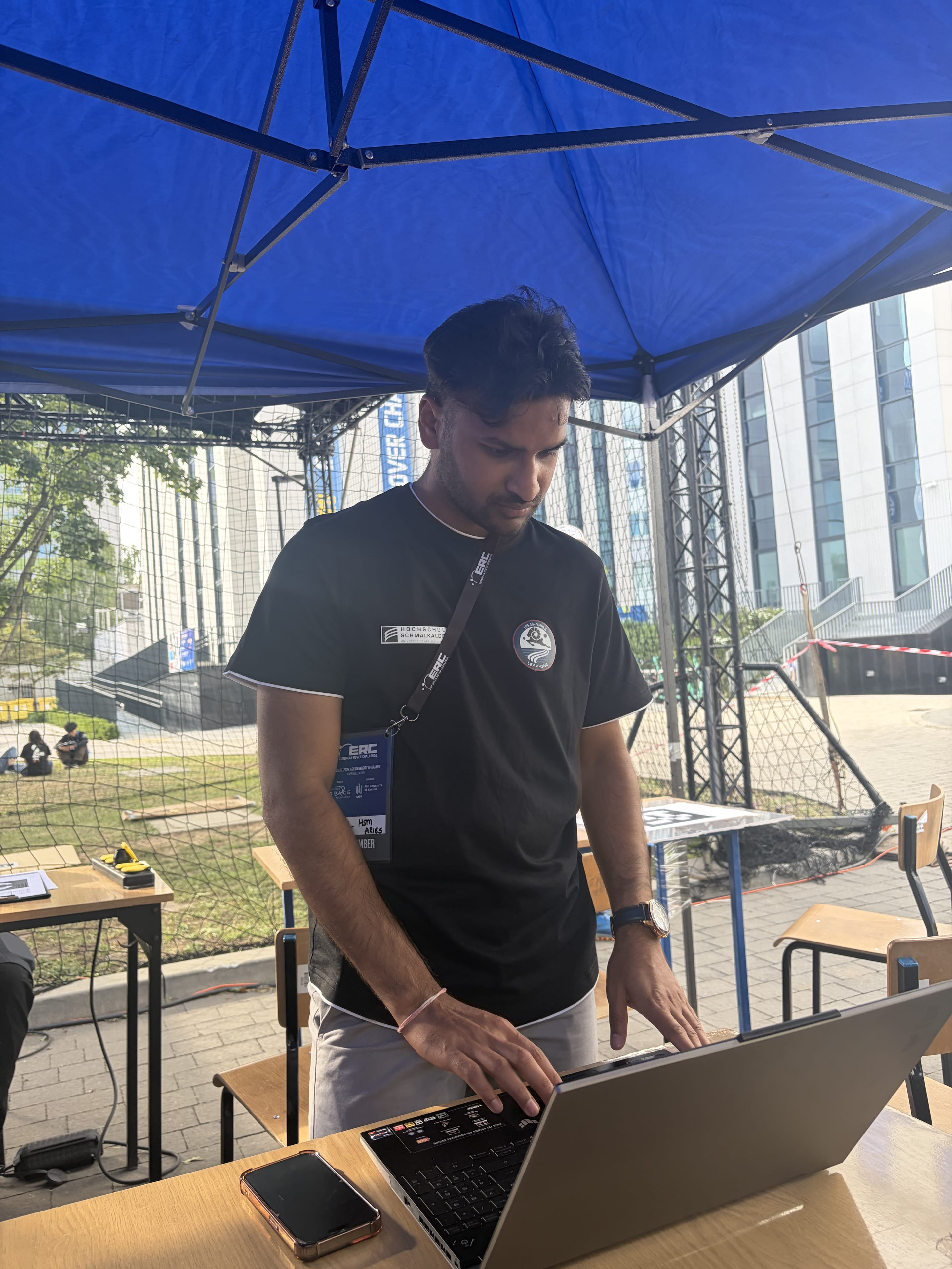 A team member works at a laptop under the pit tent with the arena netting behind.