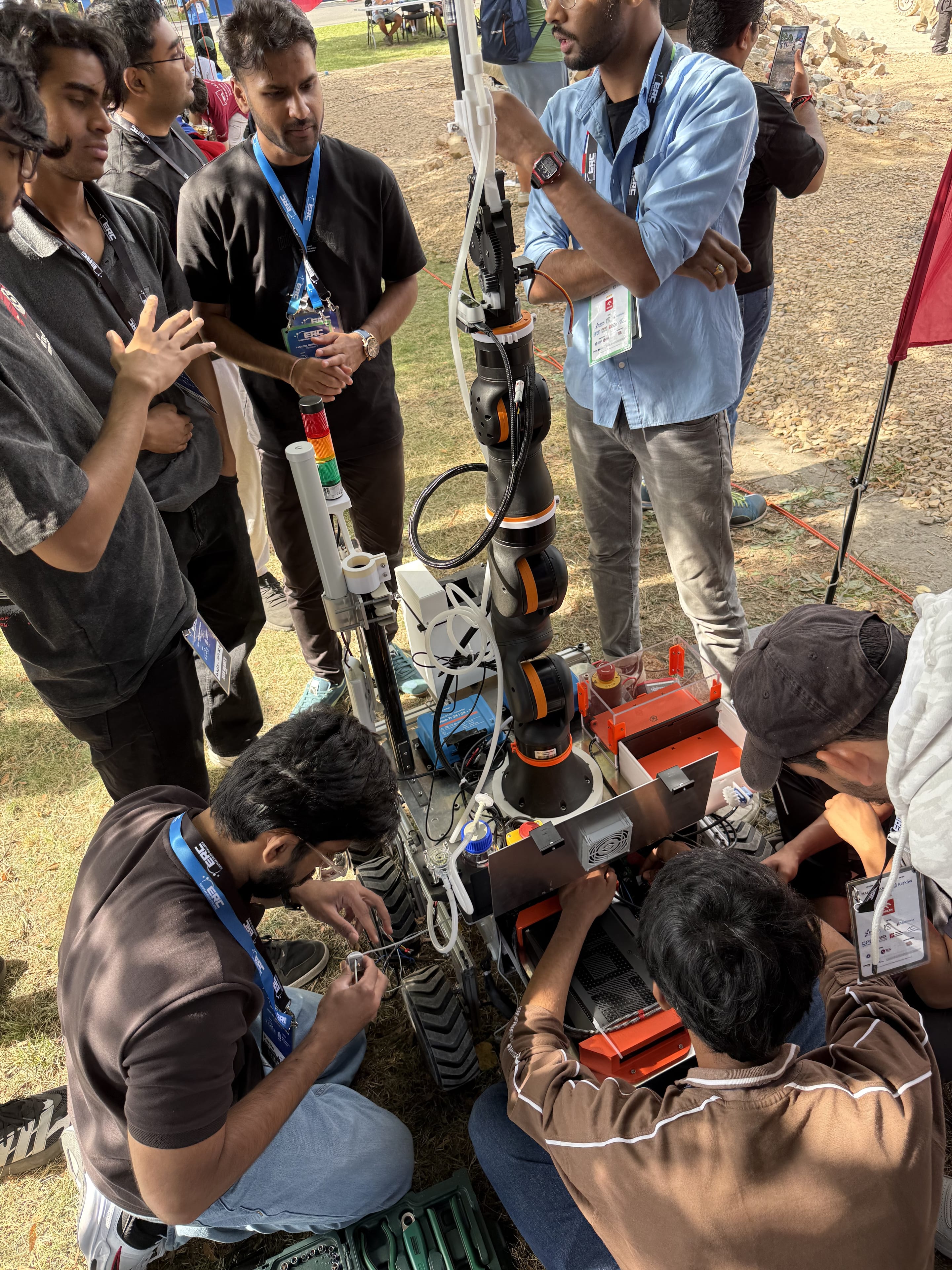 Team members repair wiring beside LEAP-One's arm and signal tower with a toolbox open on the grass.