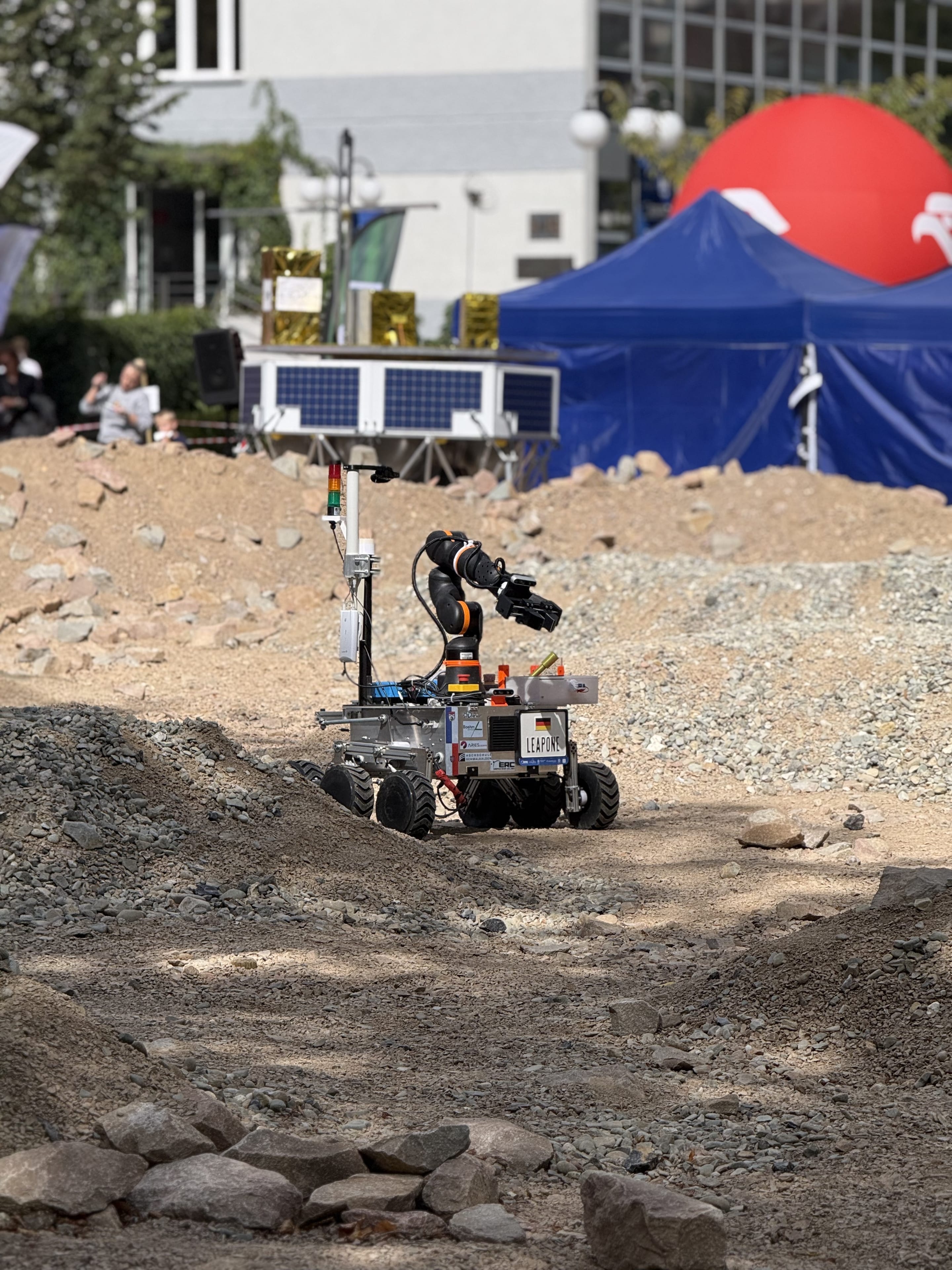 LEAP-One extends its arm on the Mars yard in front of the solar-panel stand and the red ERC dome.