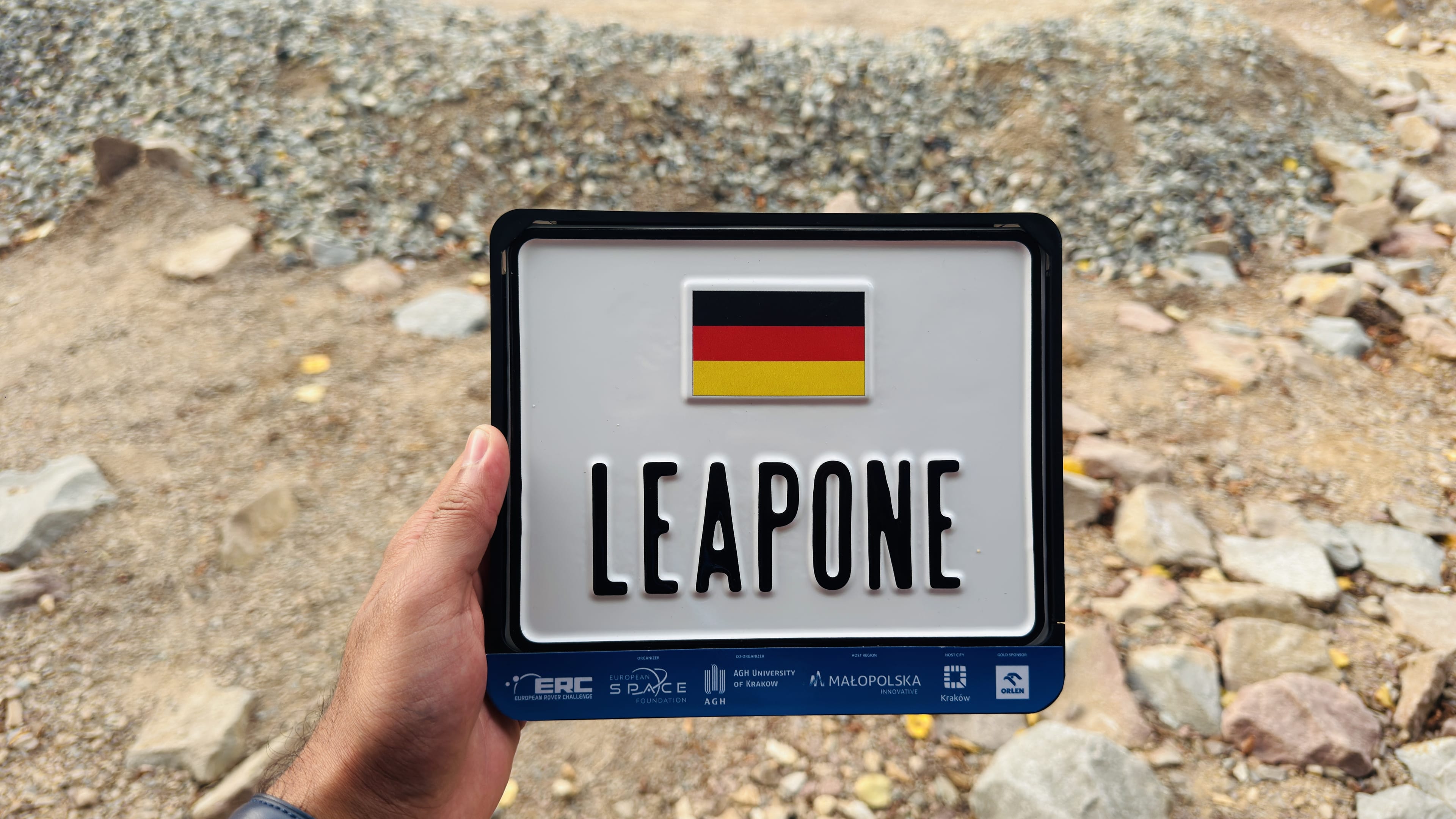 The LEAPONE competition plate is held up against the rocky Mars yard.