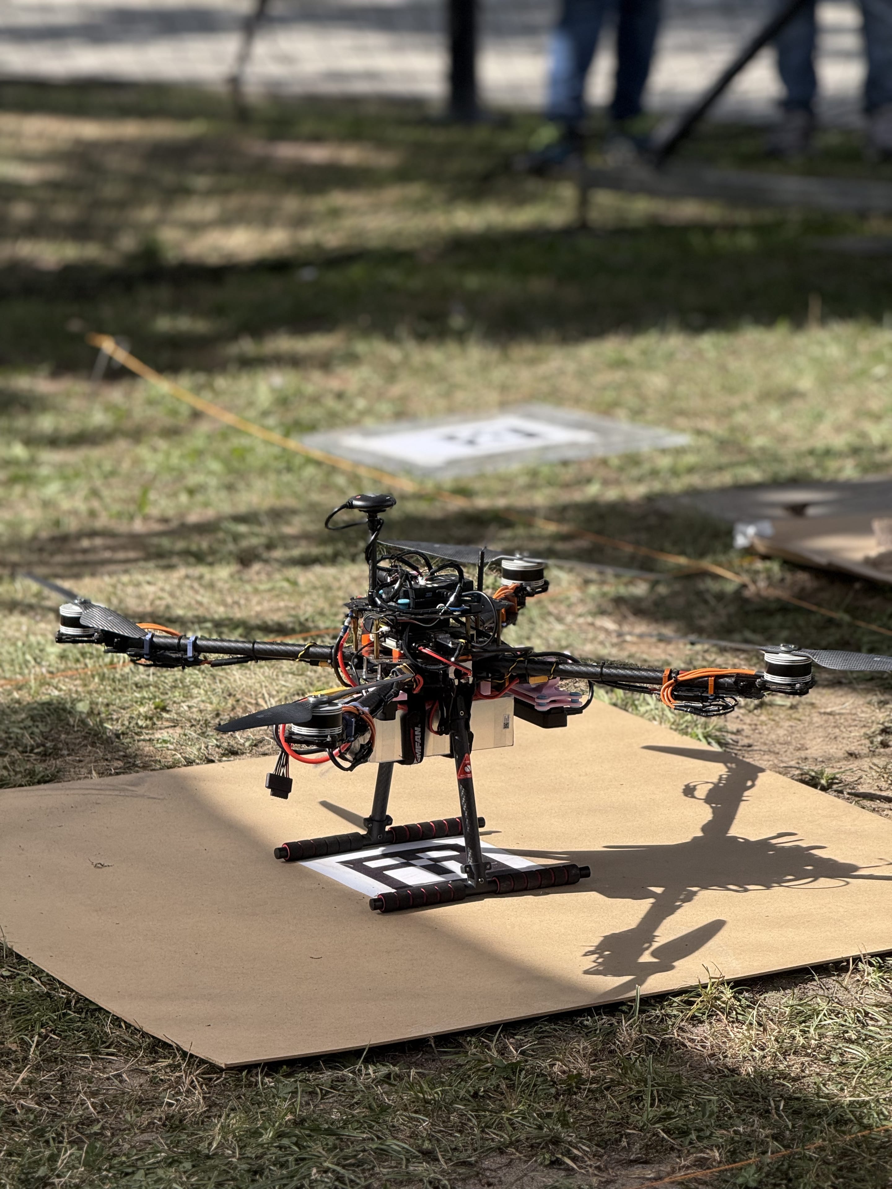 The team's quadcopter rests on its cardboard landing pad with a fiducial marker on the grass.