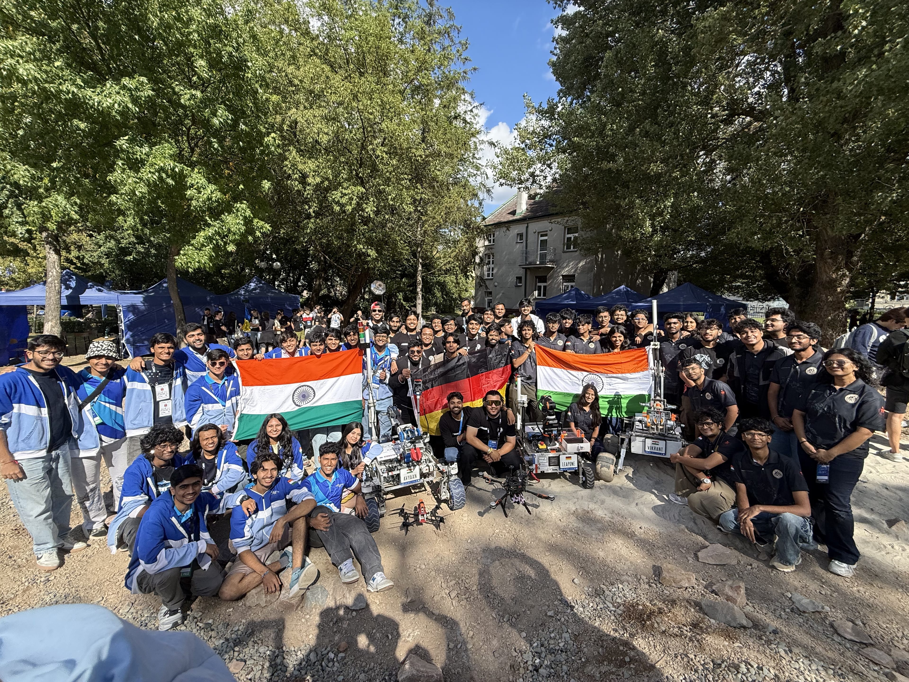 Several teams gather with their rovers and drones under Indian and German flags.
