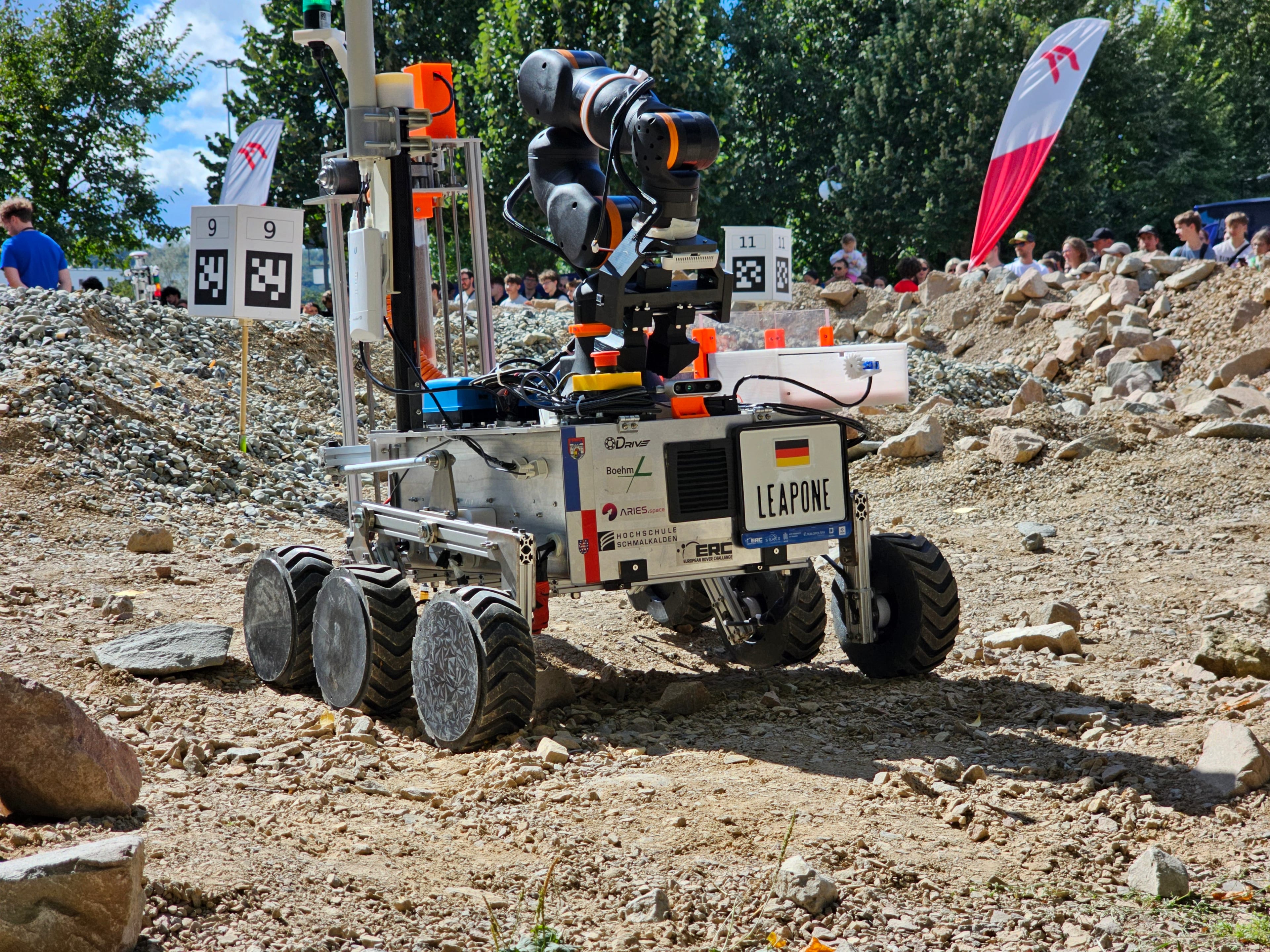 LEAP-One picks its way across the rocks of the Mars yard beside marker 9, with the crowd and the ERC flag behind.