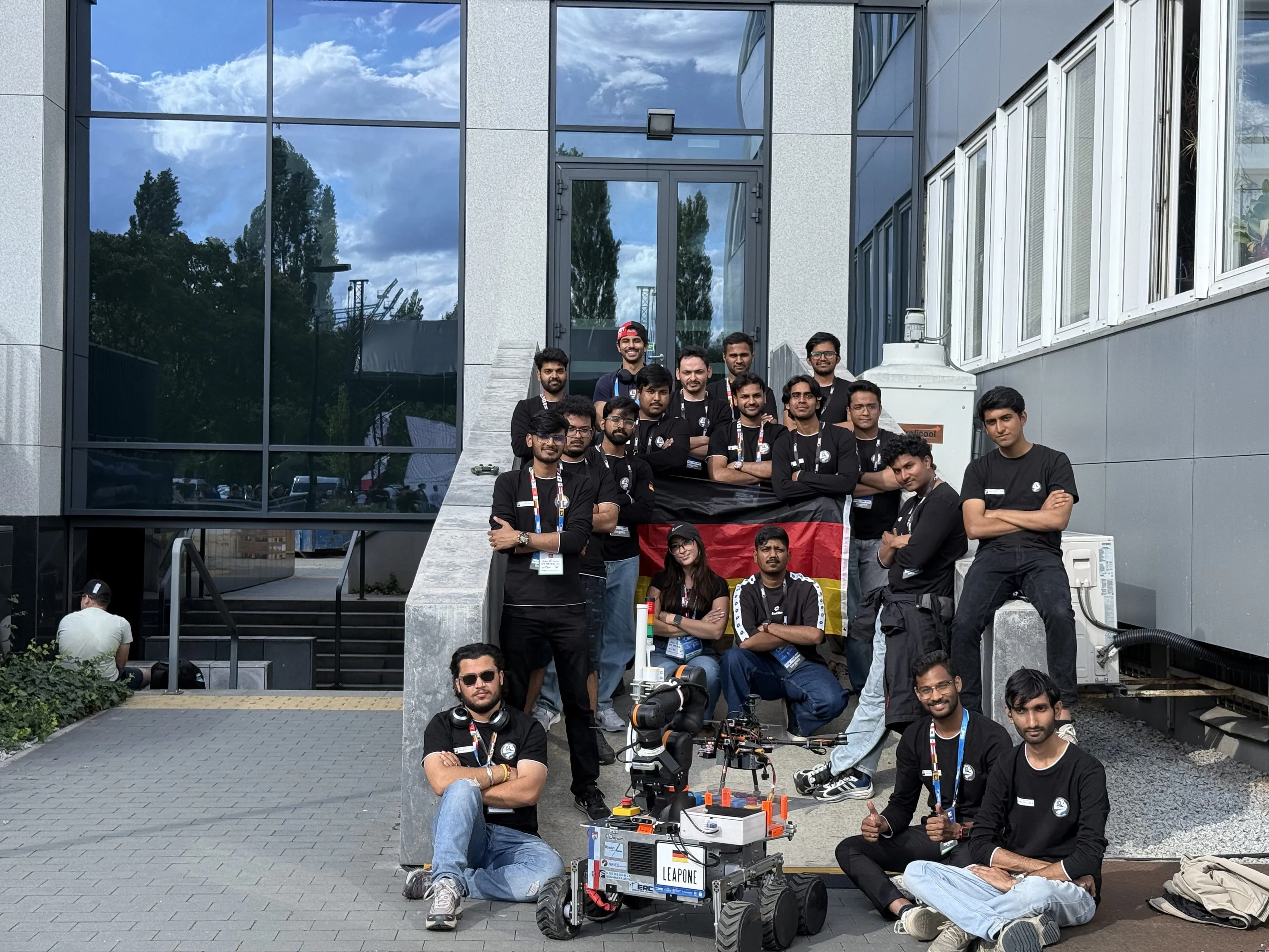 The team lines up on the steps with the German flag, LEAP-One carrying the quadcopter in front.